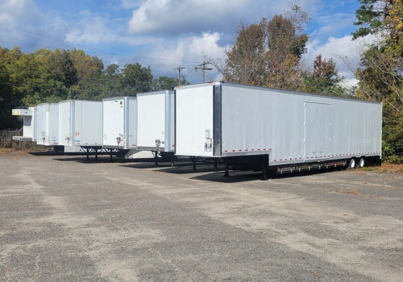 A row of white trailers parked in the middle of a lot.